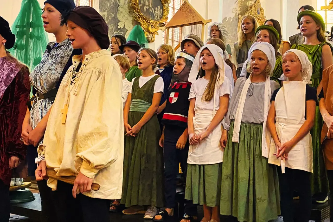 Kinder in historischen Kostümen singen.