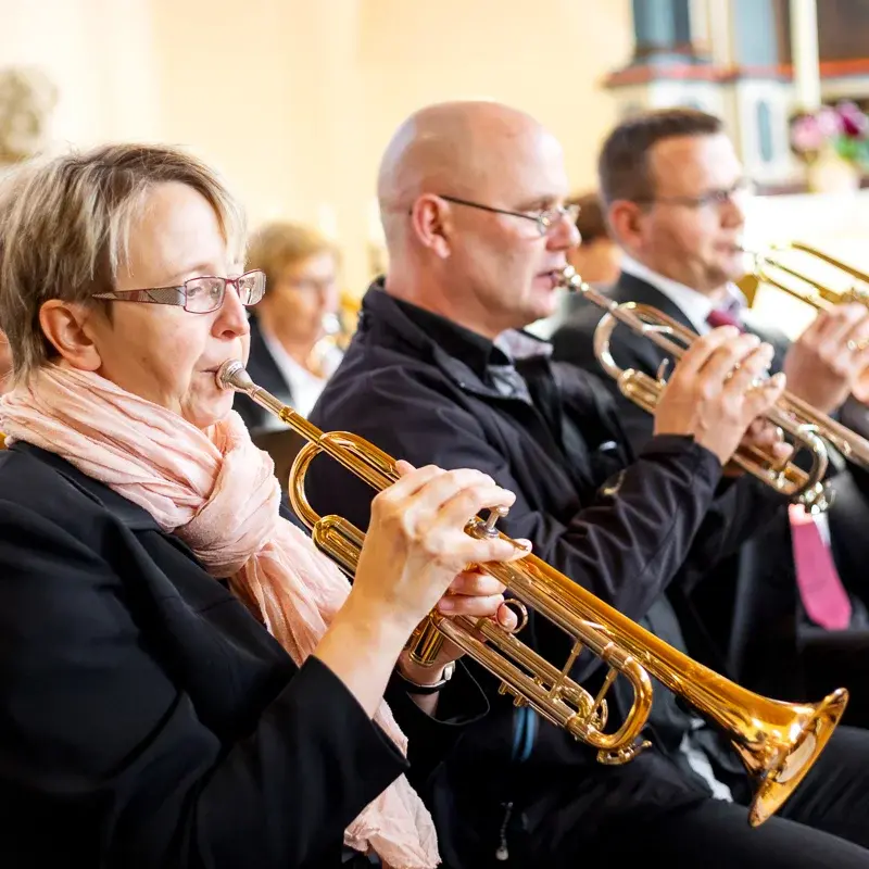 Eine Frau und zwei Männer spielen Trompete in einer Kirche.